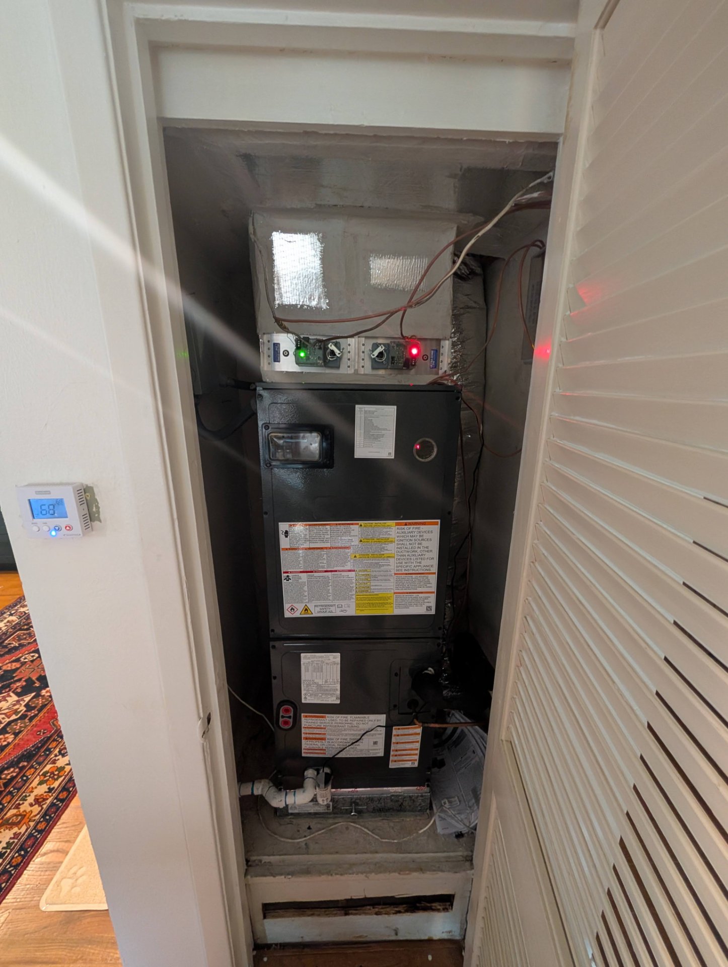 New residential HVAC air handler unit installation in a utility closet with visible ductwork and warning labels.