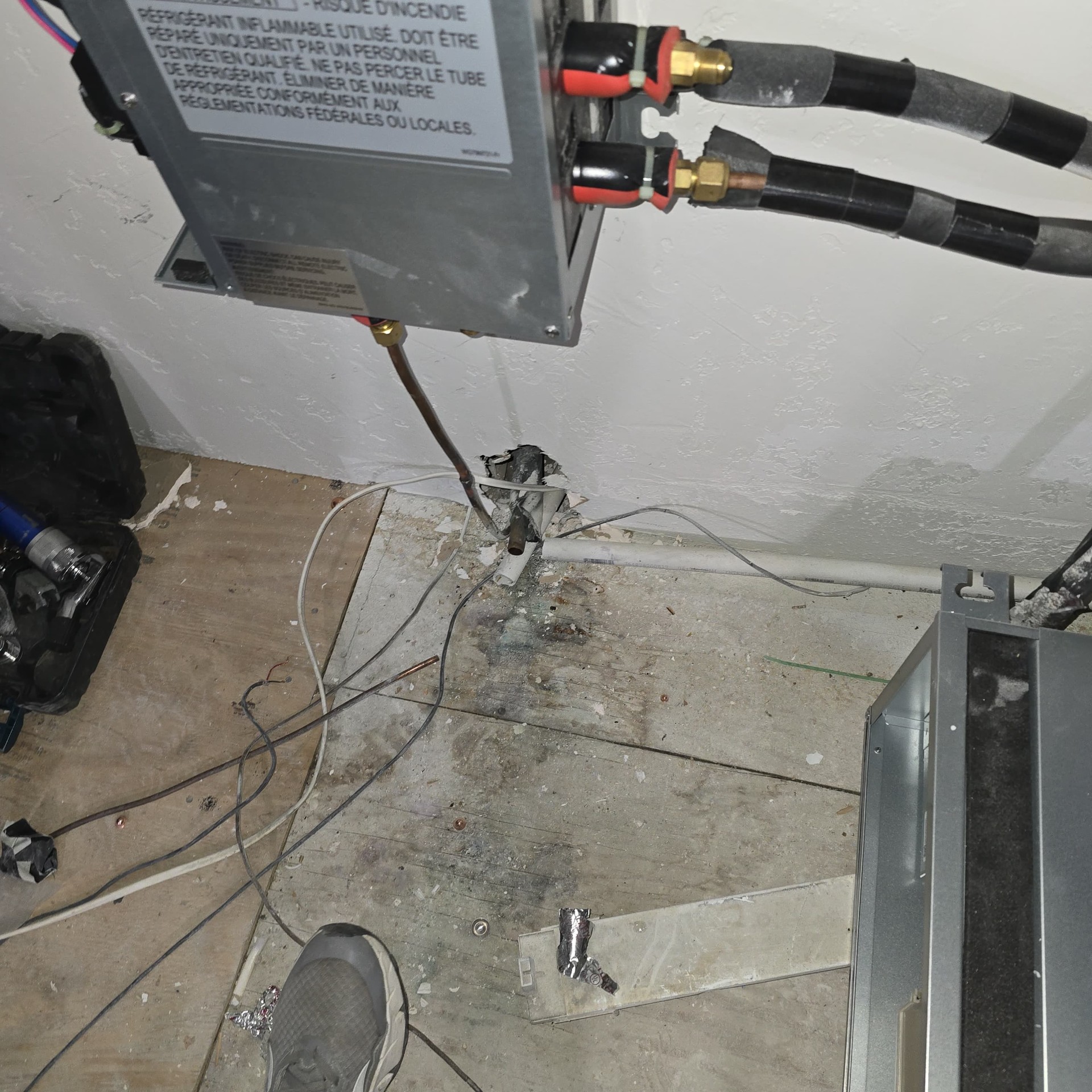 Indoor HVAC unit installation with refrigerant lines, exposed wiring, and unfinished flooring during construction.