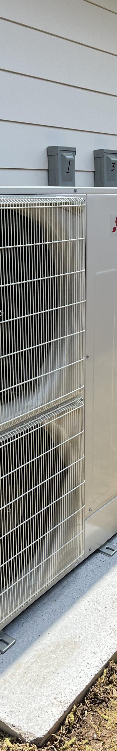 Two Mitsubishi Electric mini-split outdoor condensing units on concrete pads next to a building.