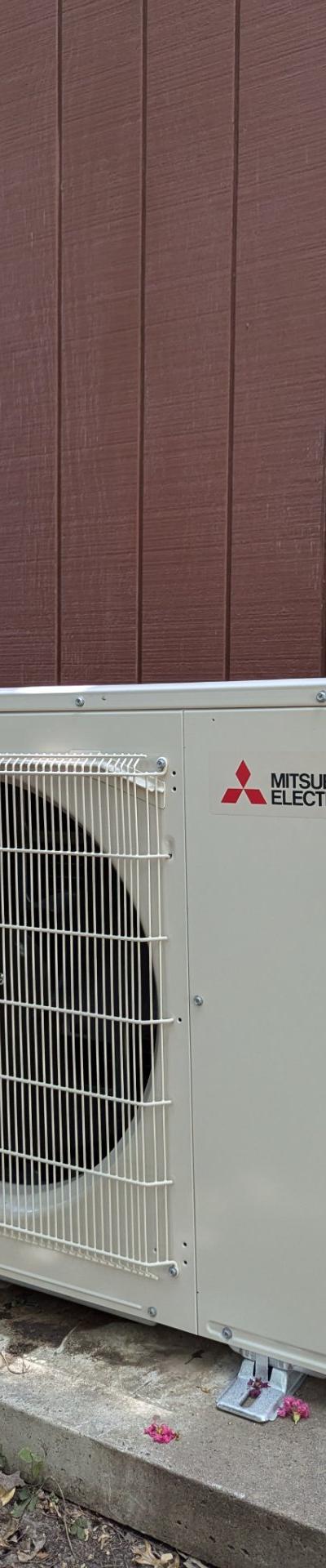 Mitsubishi Electric mini-split outdoor condenser unit on concrete pad next to a brown-sided building with conduit.