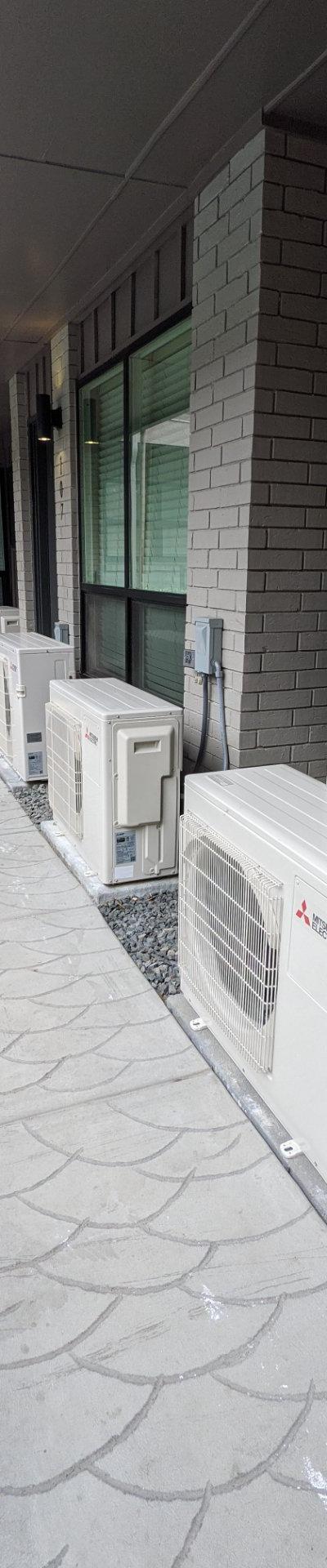 Multiple Mitsubishi Electric mini-split outdoor units installed on gravel beside a building walkway.