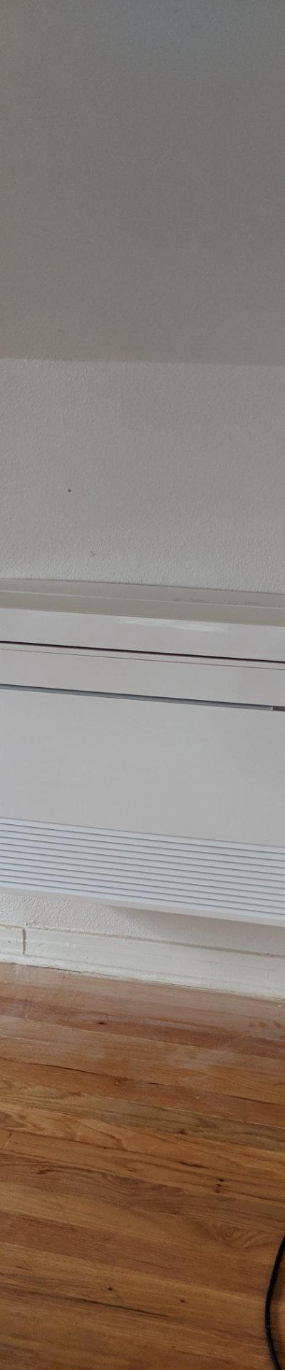 Mitsubishi Electric floor-mounted mini-split indoor unit in a room with hardwood floors and sloped ceiling.