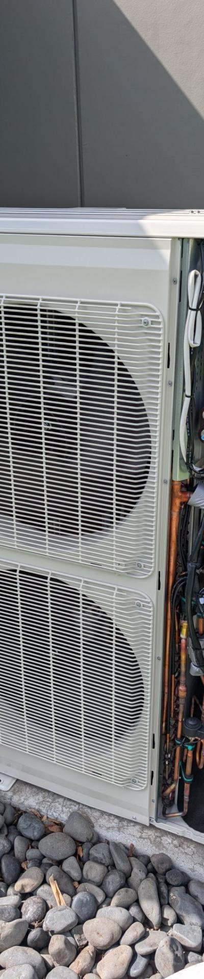 Heat pump condenser unit with side panel removed, showing internal wiring and copper lines, installed on a concrete pad.