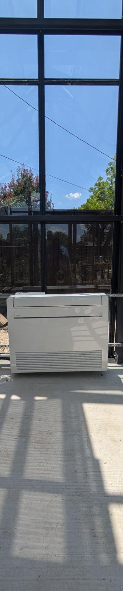 Mini-split indoor air handler installation in a sunroom with large glass panes on a concrete floor.