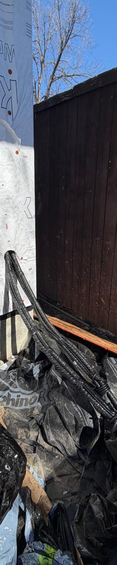 Construction wrap and discarded materials next to a wooden fence, indicating an ongoing HVAC or building project.